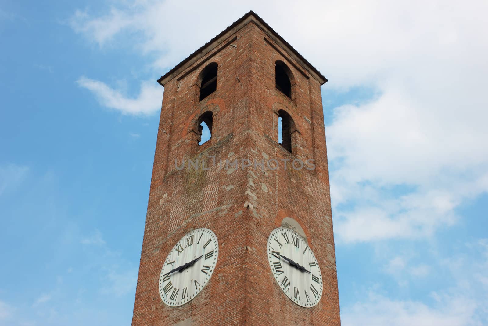 Antique clock tower in Lucca, Italy on blue sky background with white clouds.