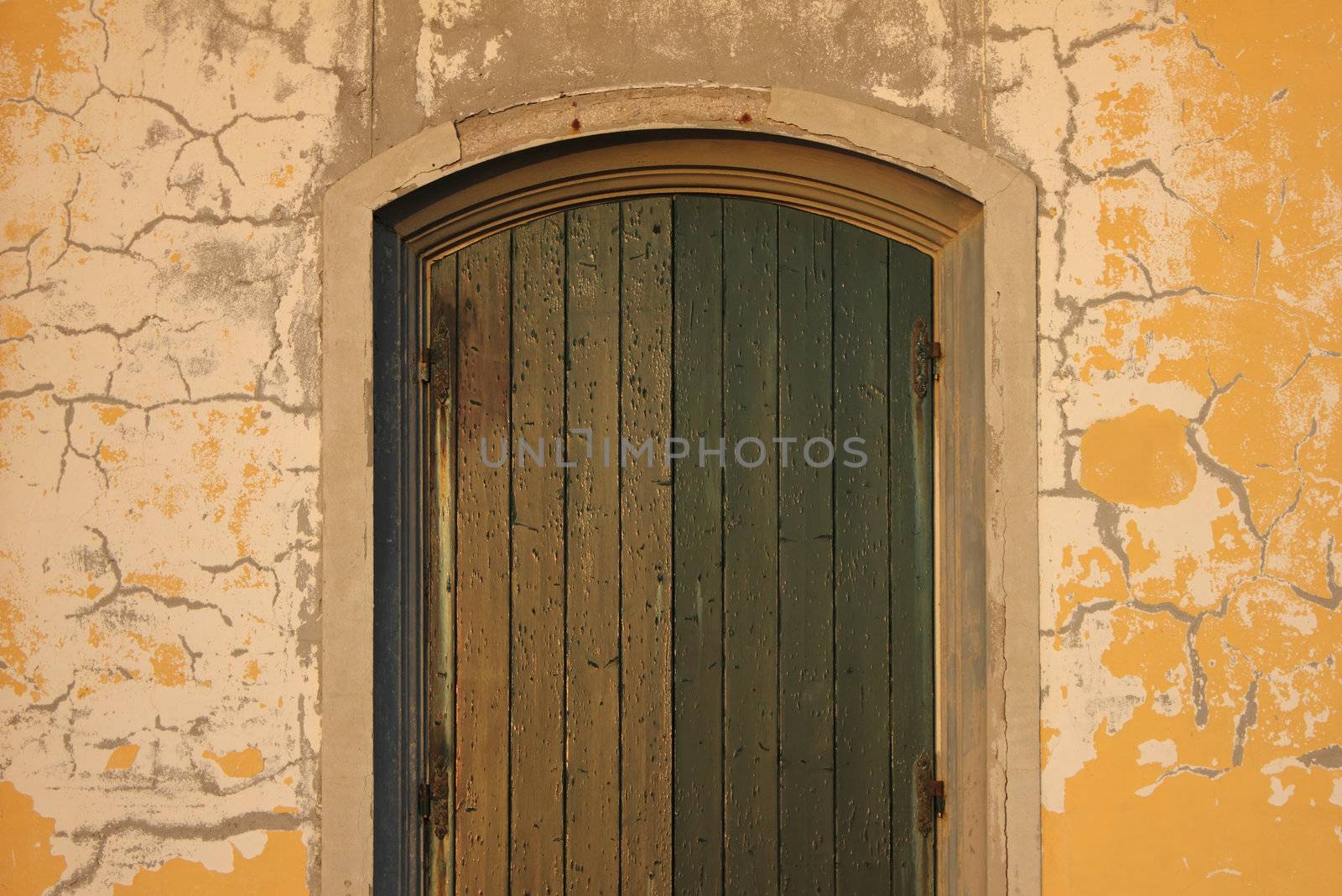 Straight shot of an old entrance door with rusty hinges and cracks on the wall. 