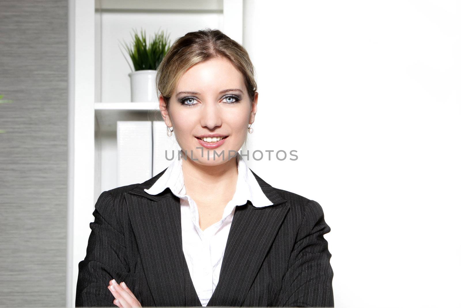 Smiling confident professional woman standing in her office looking at the camera with her arms folded