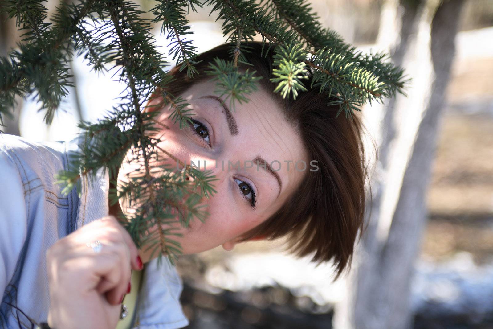Portrait of beautiful young girl under spruce tree and looking to camera