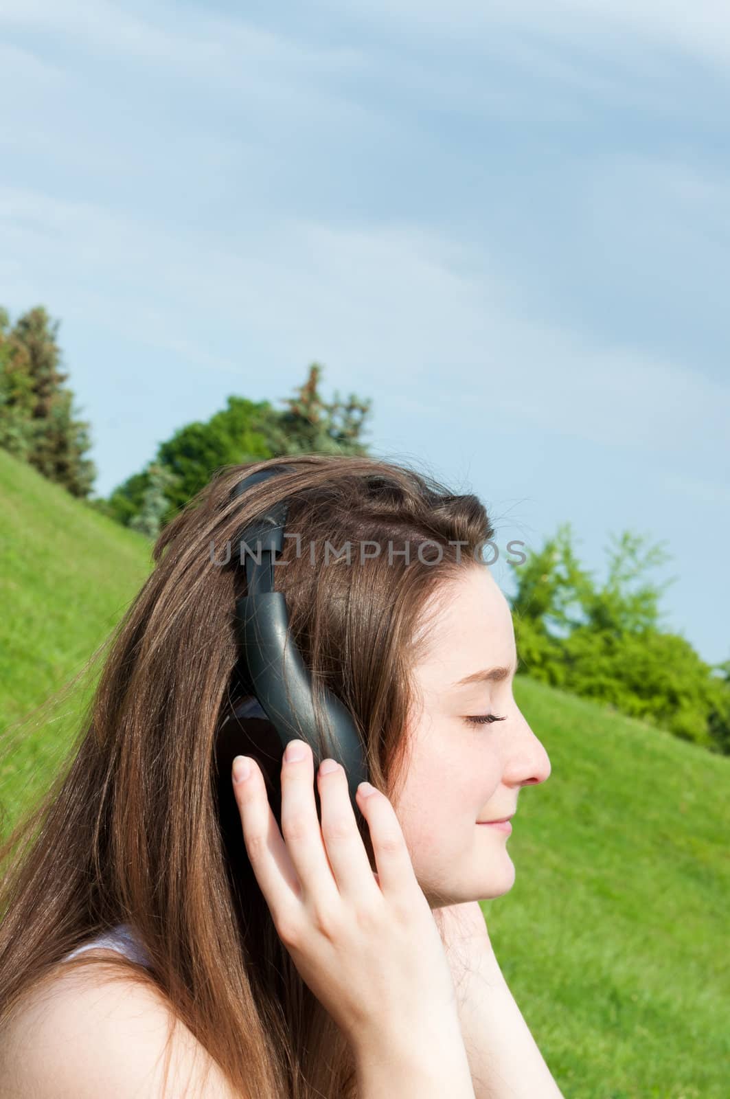 Young girl listens to music headphones summer in park.