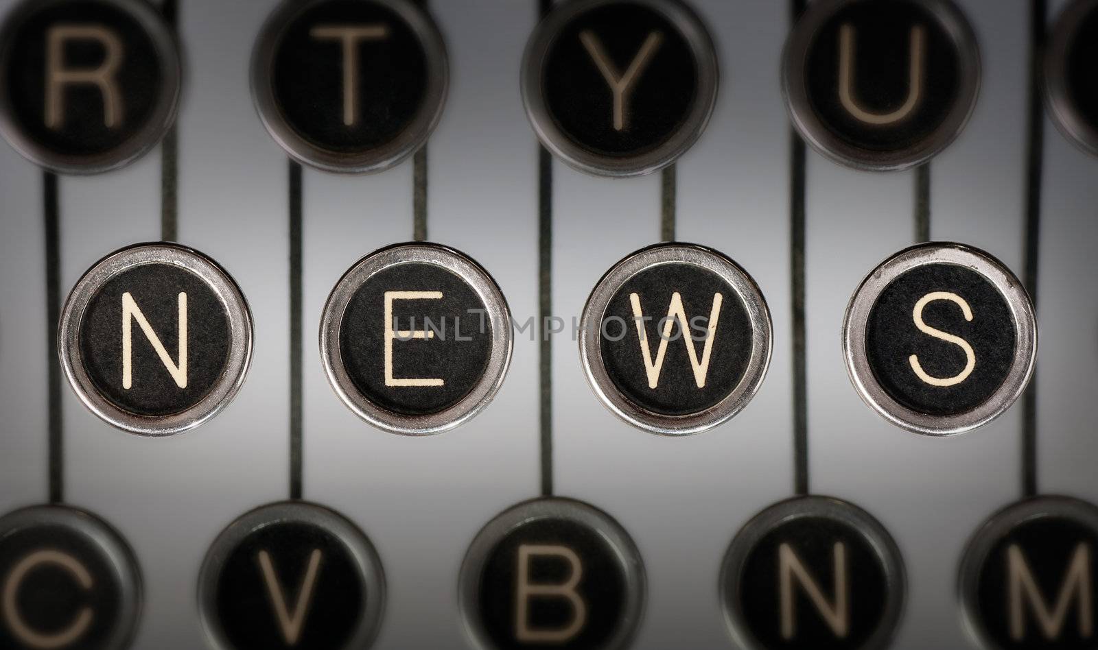 Close up of old typewriter keyboard with scratched chrome keys with black centers and white letters. Lighting and focus are centered on for keys spelling out "NEWS". 