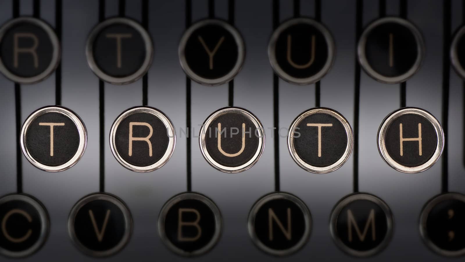 Image of old typewriter keyboard with scratched chrome keys that spell out the word "TRUTH". Lighting and focus are centered on "TRUTH".
