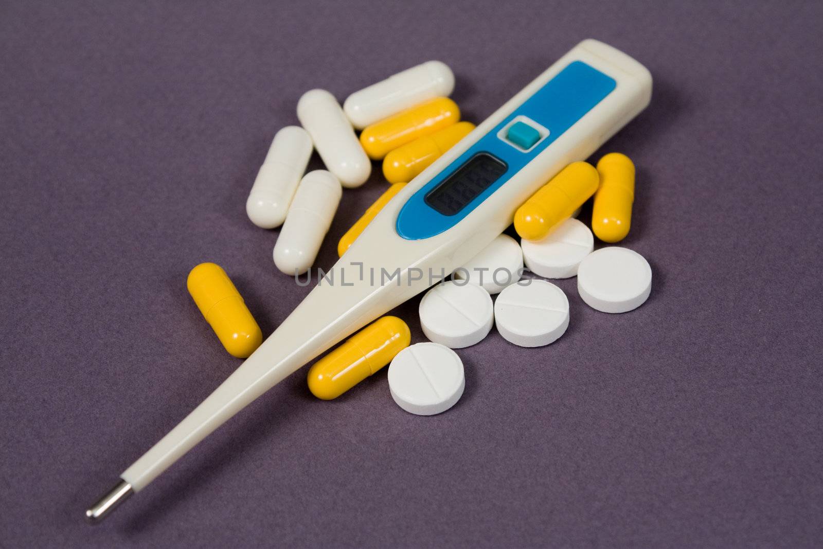 White tablets, white and yellow pills and an electronic thermometer
