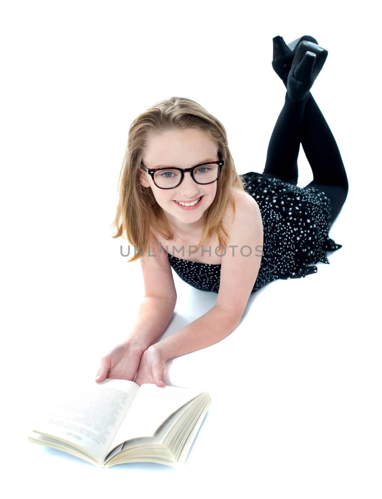 Smiling little girl lying with an open book on floor. All on white background