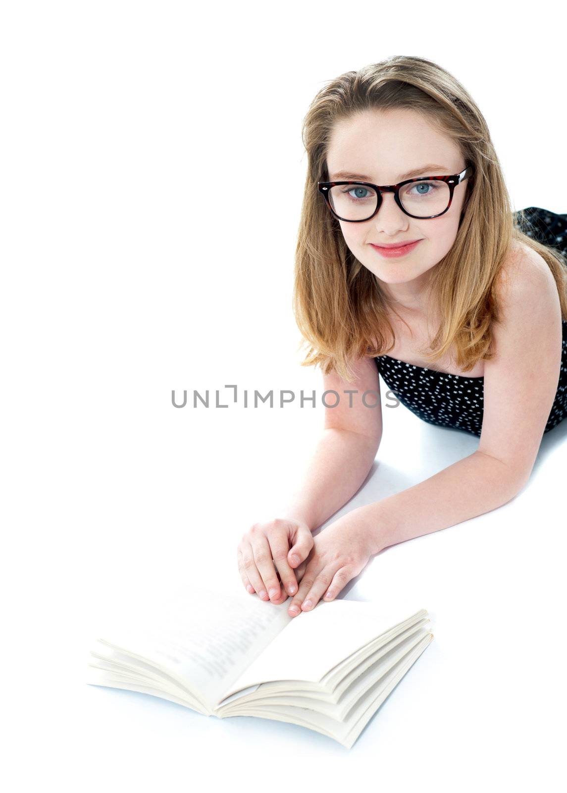 Girl wearing eyeglasses and reading book. Lying on white floor
