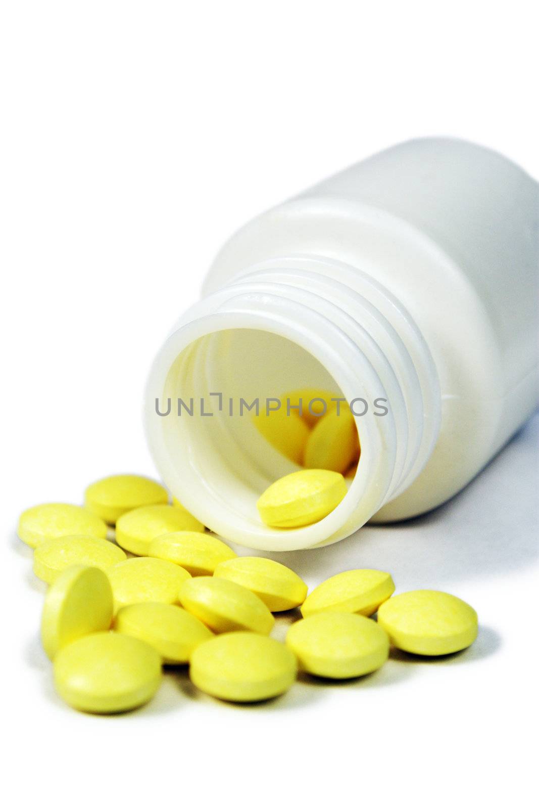 Overturned plastic jar of yellow pills on white background