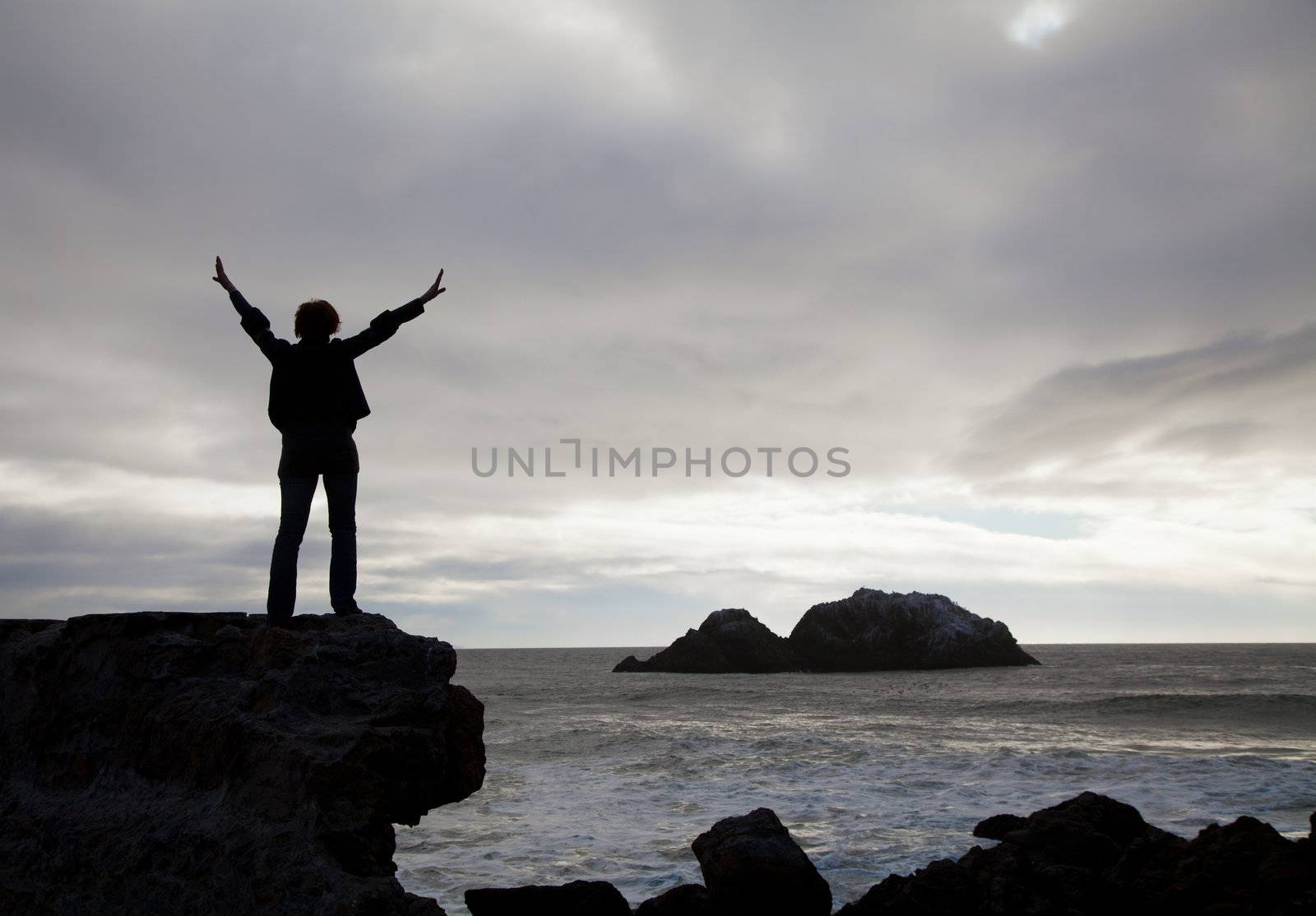Woman staying with raised hands against sunset at the ocean