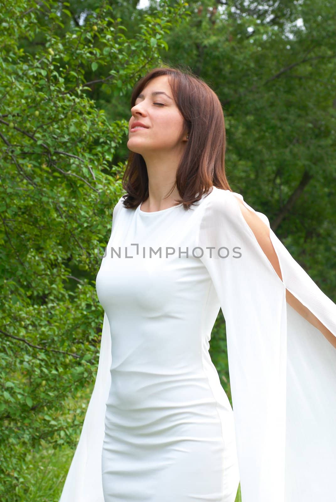 young happy caucasian brunette woman in white dress enjoying in wind with closed eyes