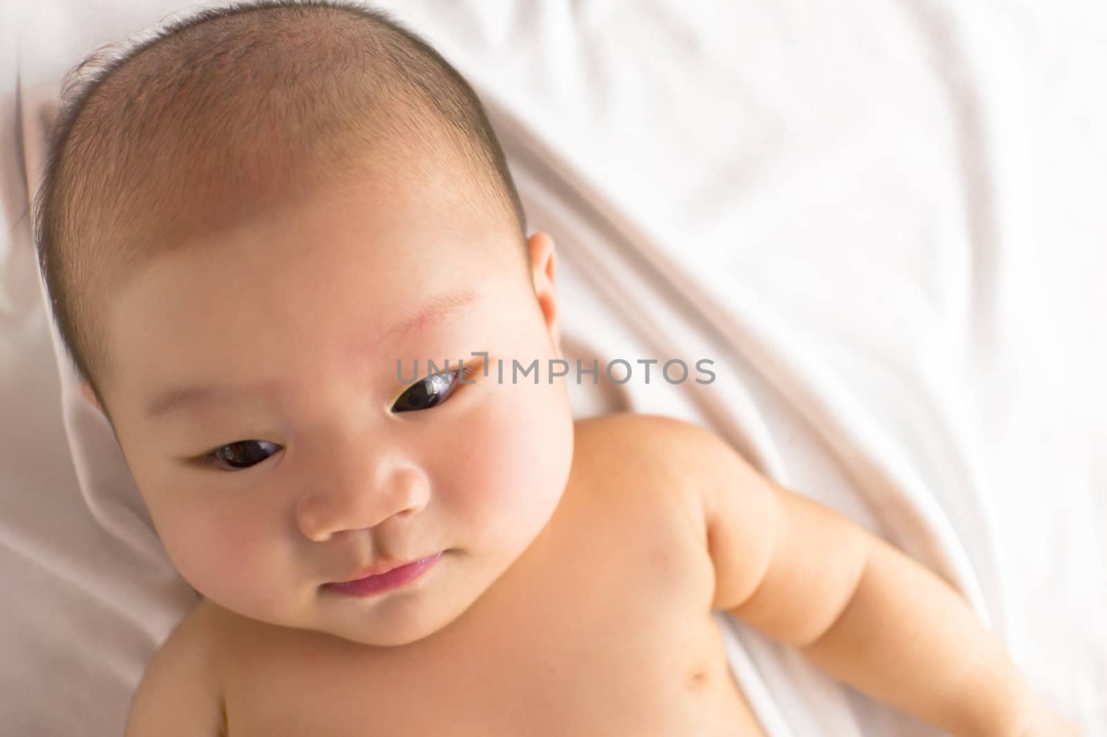 A cute asian baby resting on the bed looking down