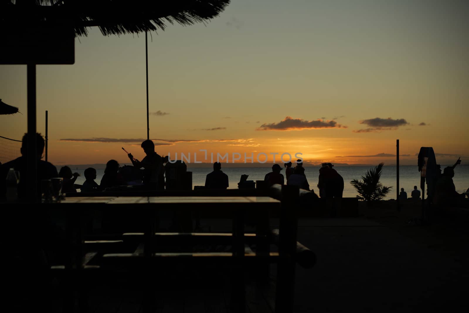 Tourists silhouette sitting along the seashore over the sunset background