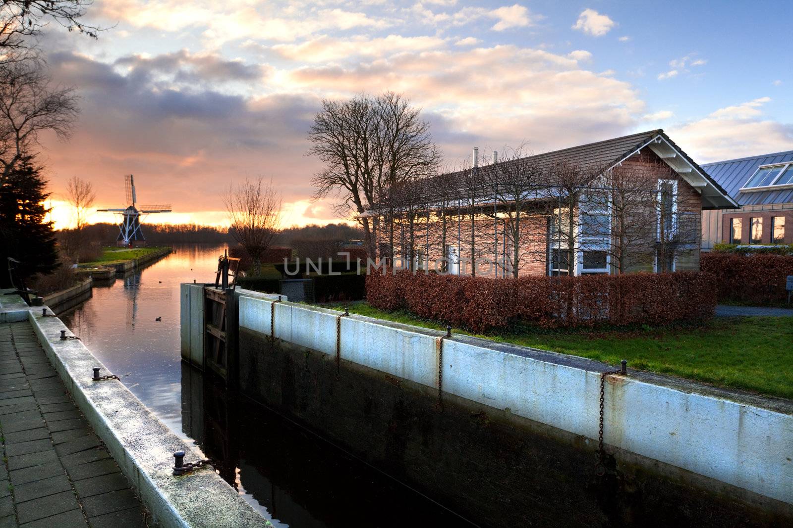 view on Dutch village before the sunset, with small channel, windmill and farms