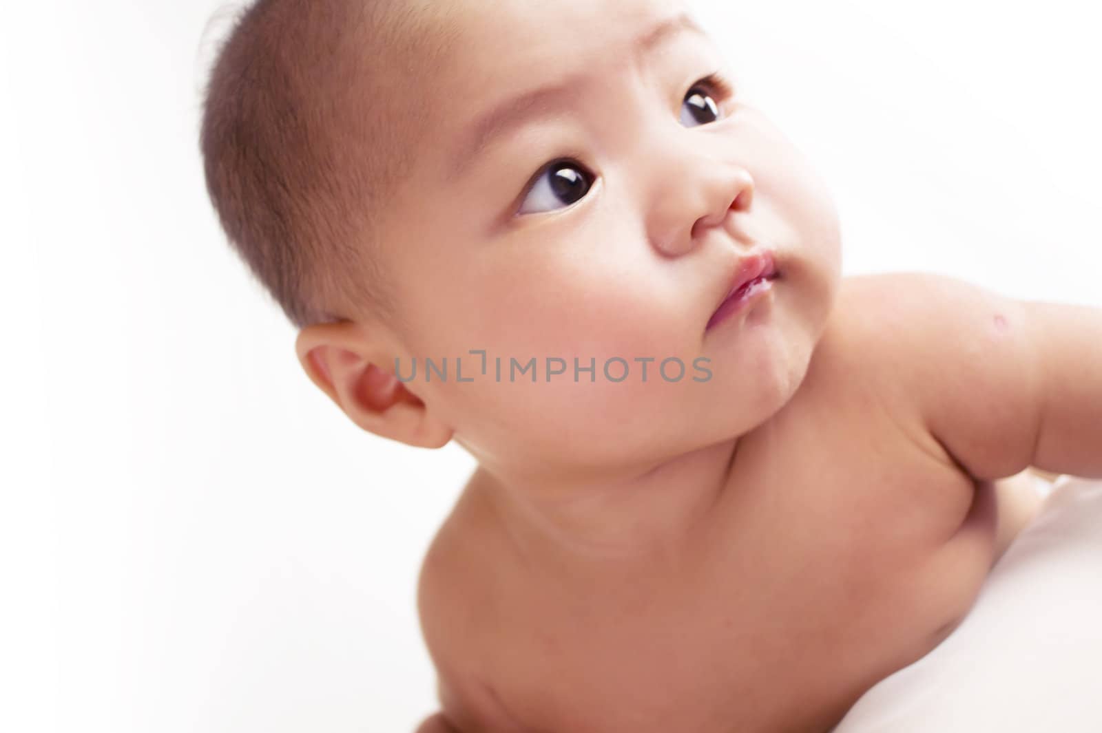 A cute asian baby laying stomach down on the bed with white background