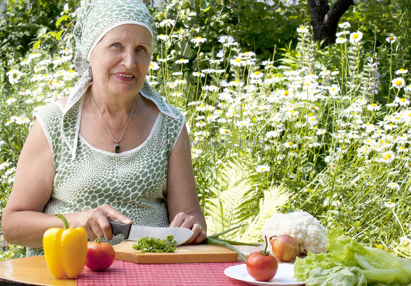The adult woman with a smile cuts salad from fresh appetizing vegetables