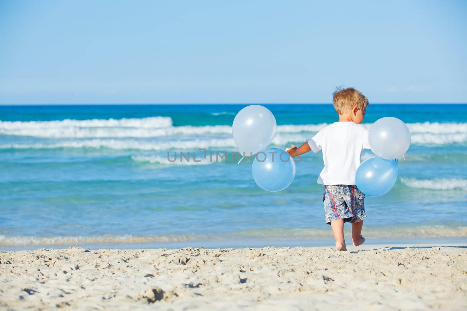 Back vie of cute little boy plays with ballons on the beach