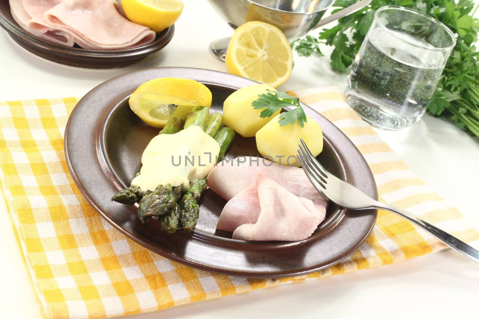 green Asparagus with hollandaise sauce, potatoes and cooked ham on a light background