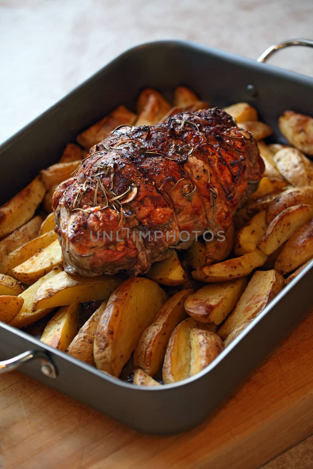 Photo of a lamb roast with potatoes in a roasting pan fresh out of the oven.
