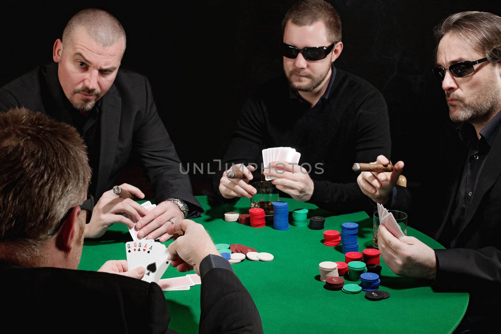 Photo of four men playing poker, smoking cigars and drinking whiskey. Focus is on the winning hand.