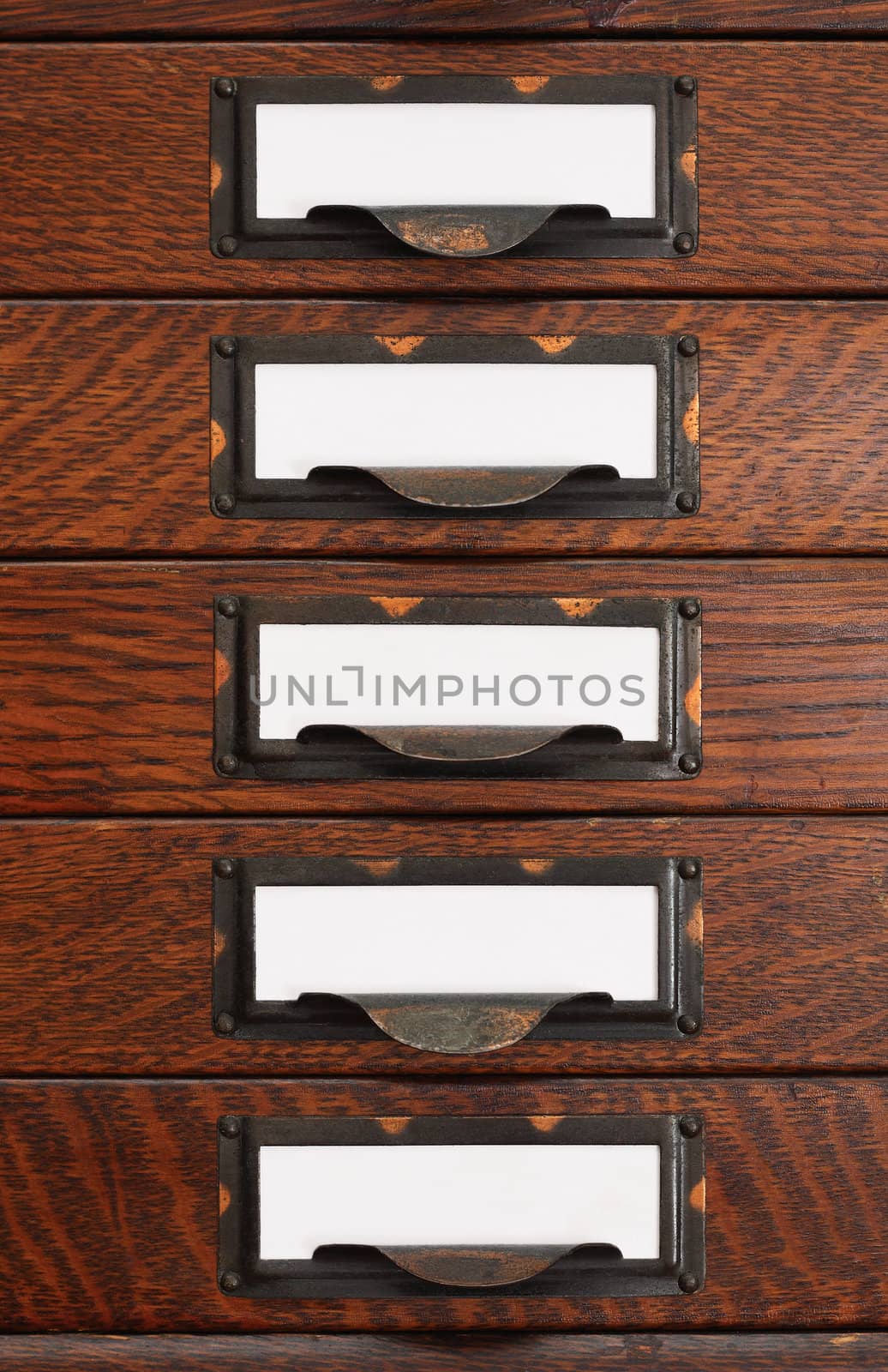 Vertical stack of five old oak flat file drawers with white empty tags in tarnished brass label holders.
