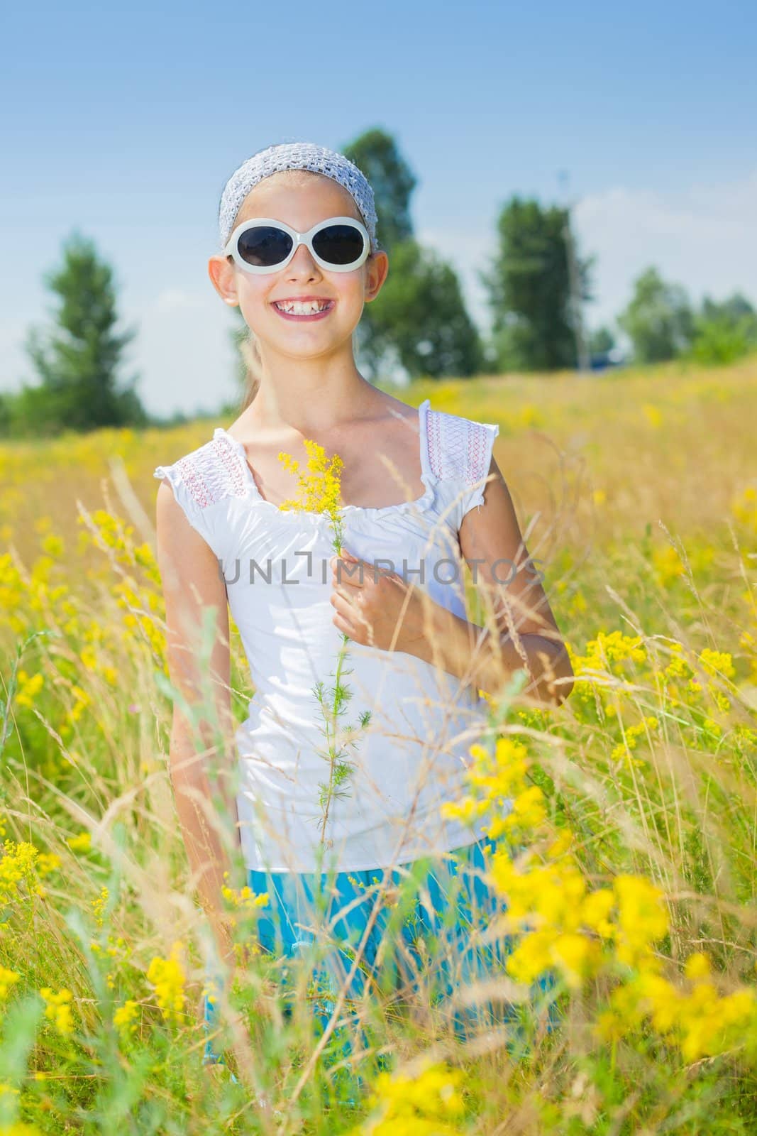 Adorable girl in glasses with flowers in yellow field. Summer freedom andjoy concept. Vertical view