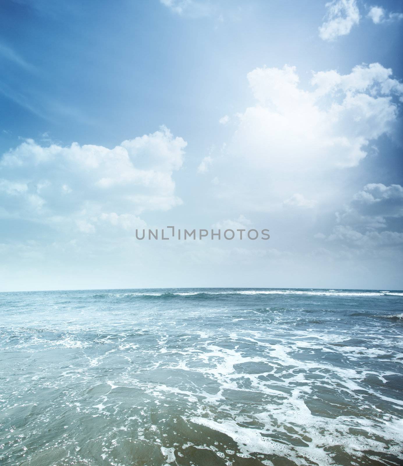 Vertical photo of the blue sea with foam and cloudy sky. Vibrant colors