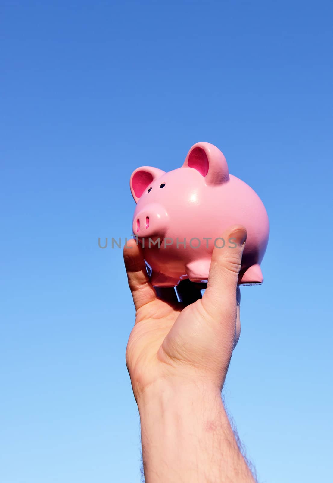 holding up a piggy bank against a pure blue sky background