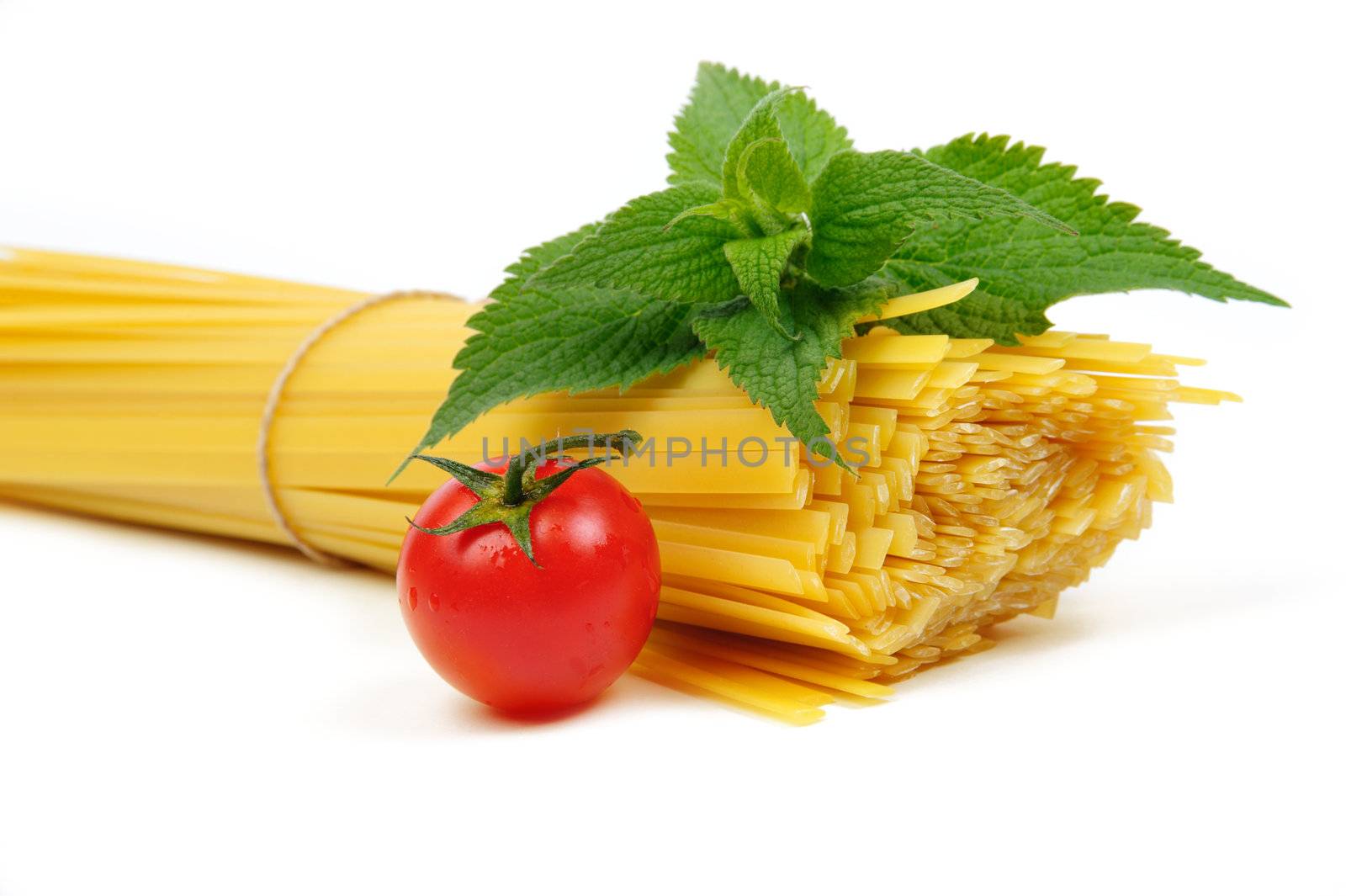 An image of raw yellow pasta, tomato and green leaves