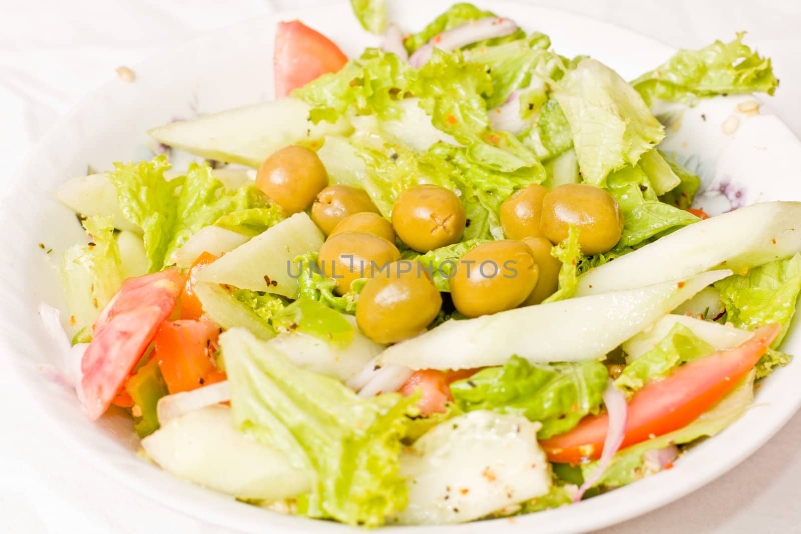 A tasty salad with tomatoes, green olives, onions and lettuce served in a bowl