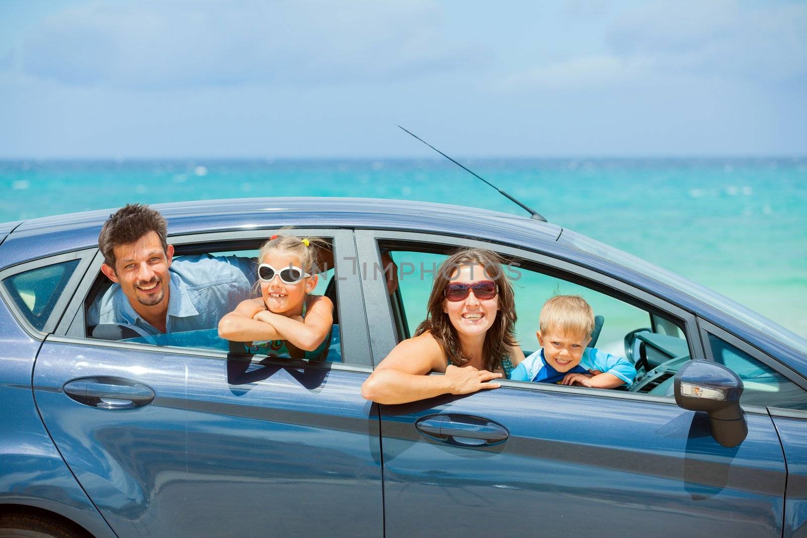 A family of four, mother, father, son and daughter driving in a car on a sunny day in hot location, backround sea