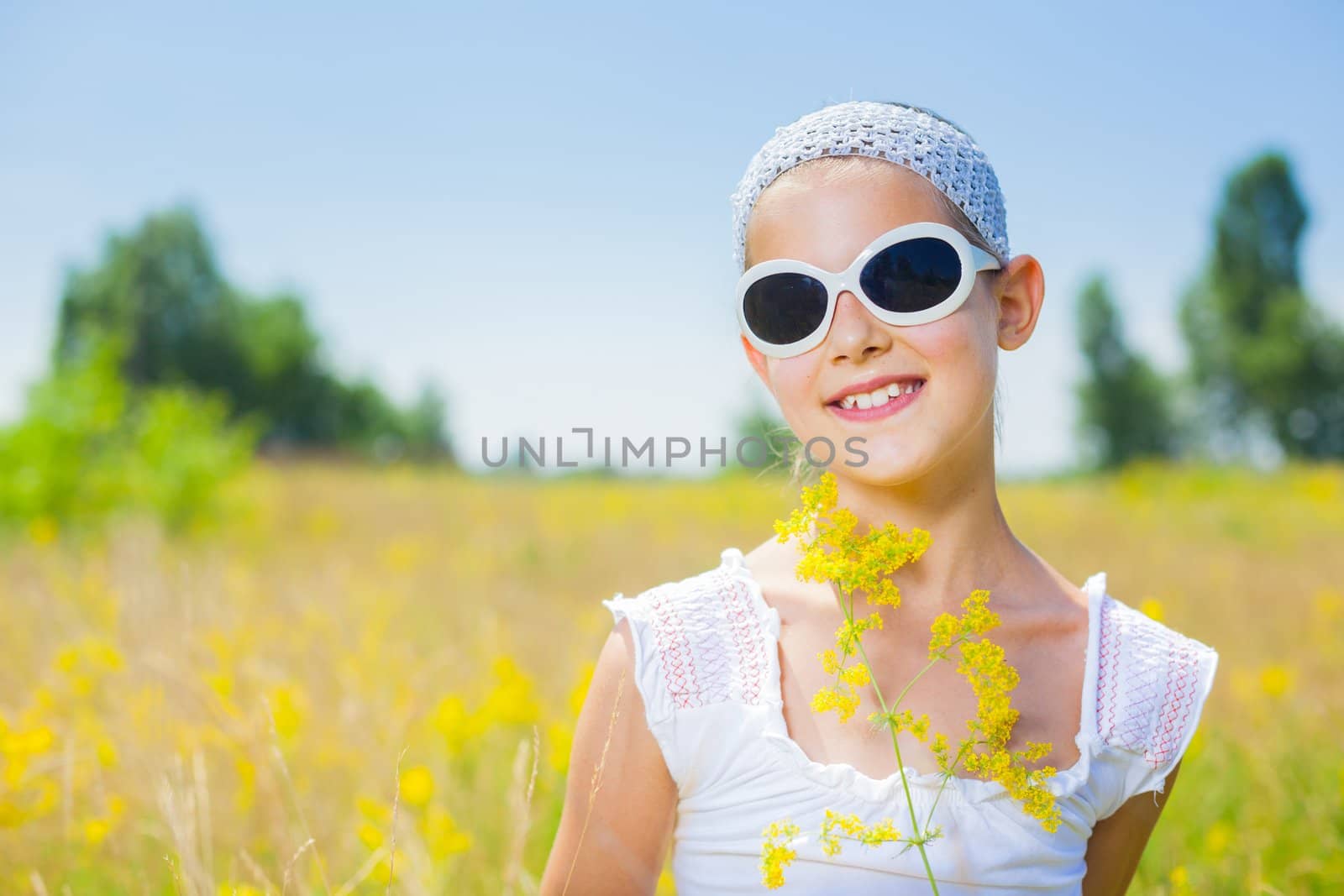 Adorable girl in glasses with flowers in yellow field. Summer freedom andjoy concept.
