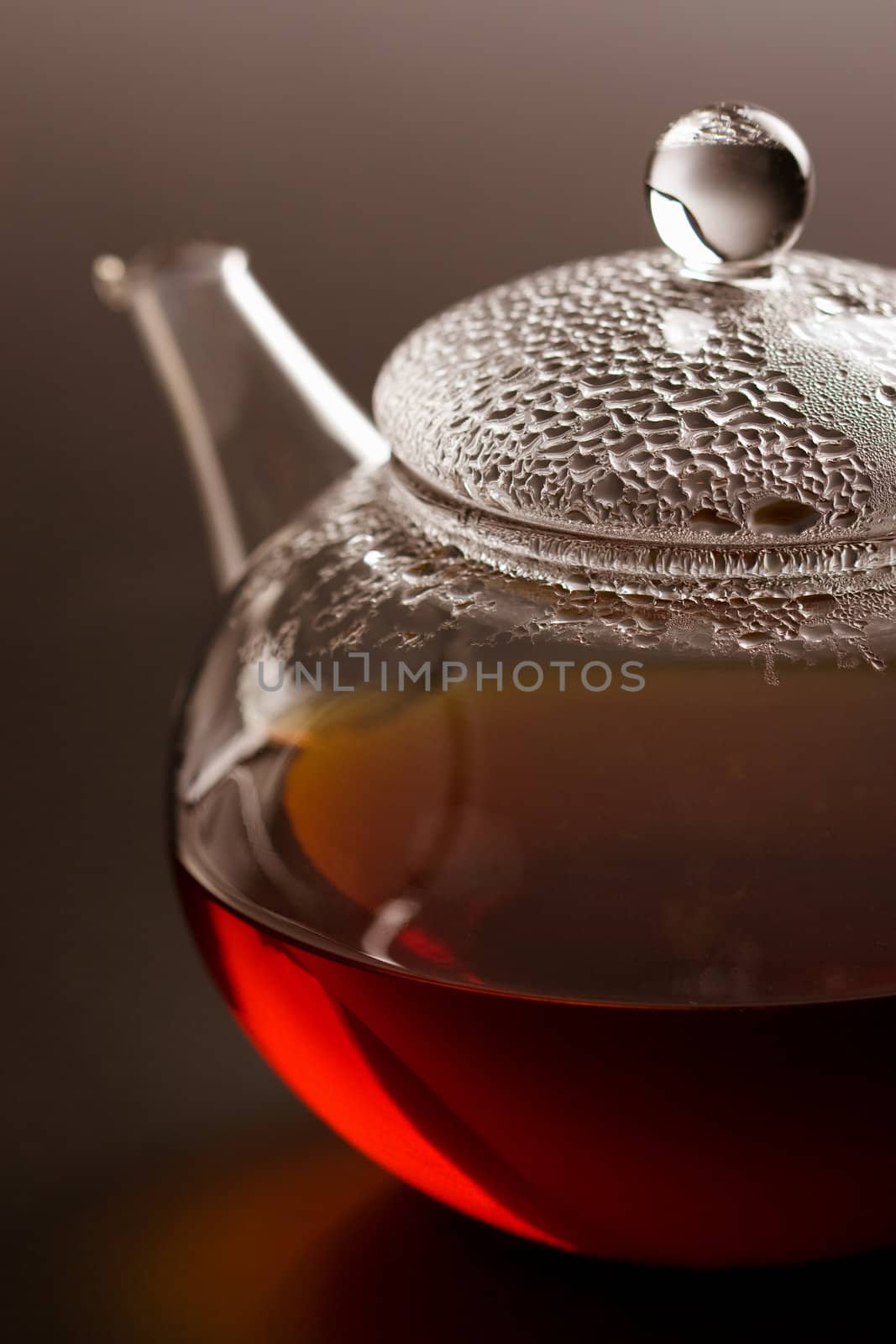 transparent teapot with black tea over dark background
