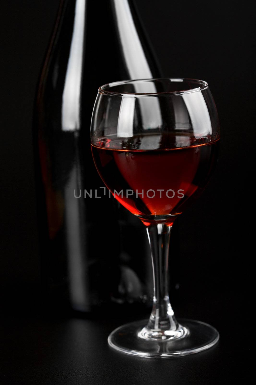 glass of red wine and bottle over black background