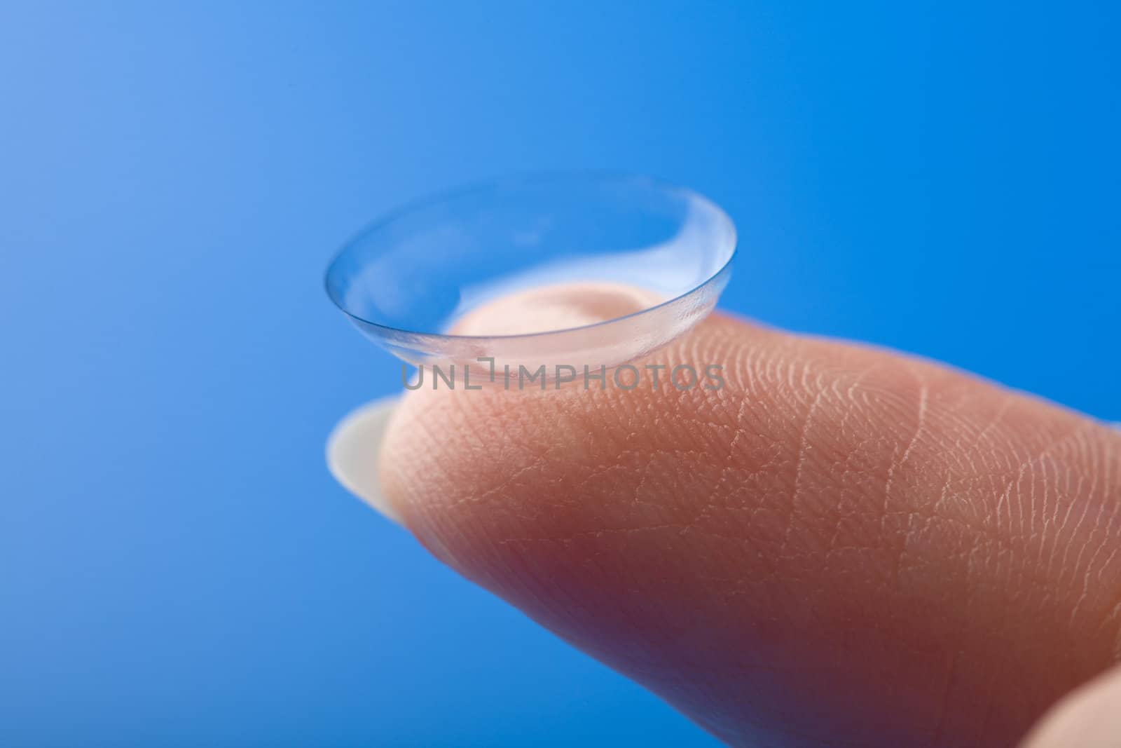 finger holding contact lens over blue background
