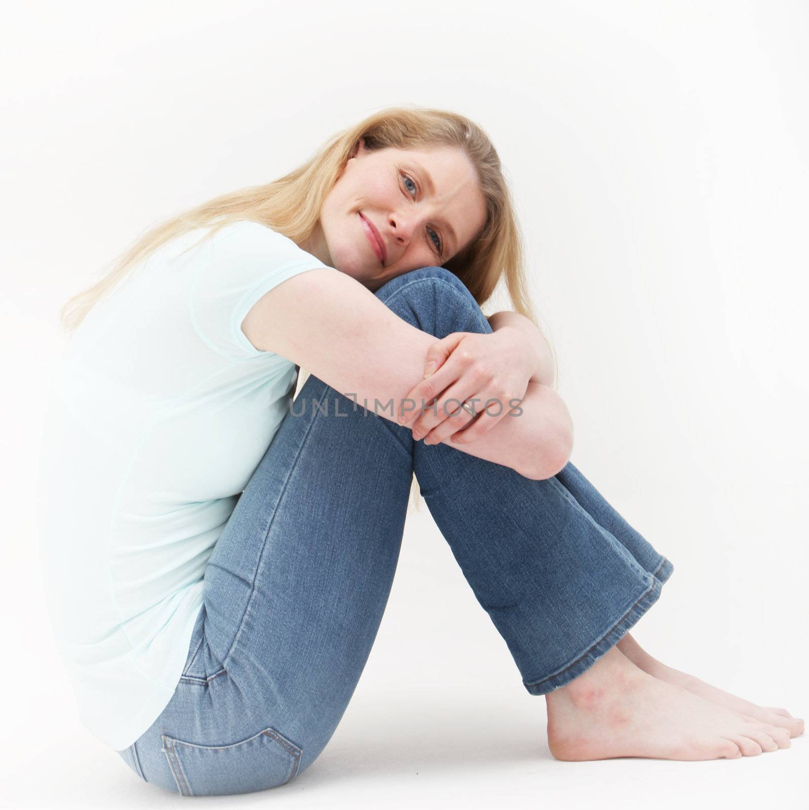 Contentment shown by a pretty blonde girl while hugging her knees seated on the floor