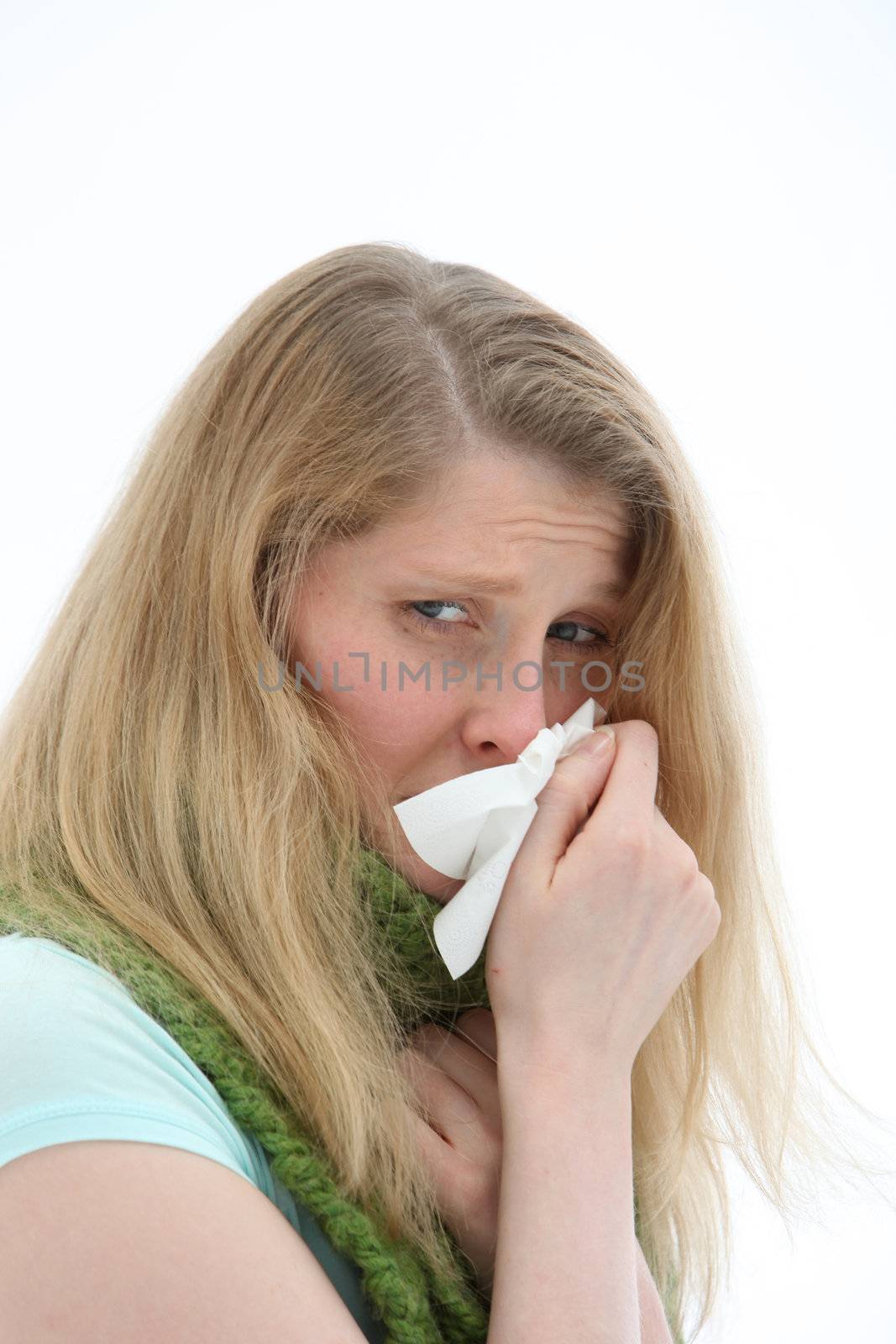 Young girl with a miserable head cold blowing her nose in a tissue