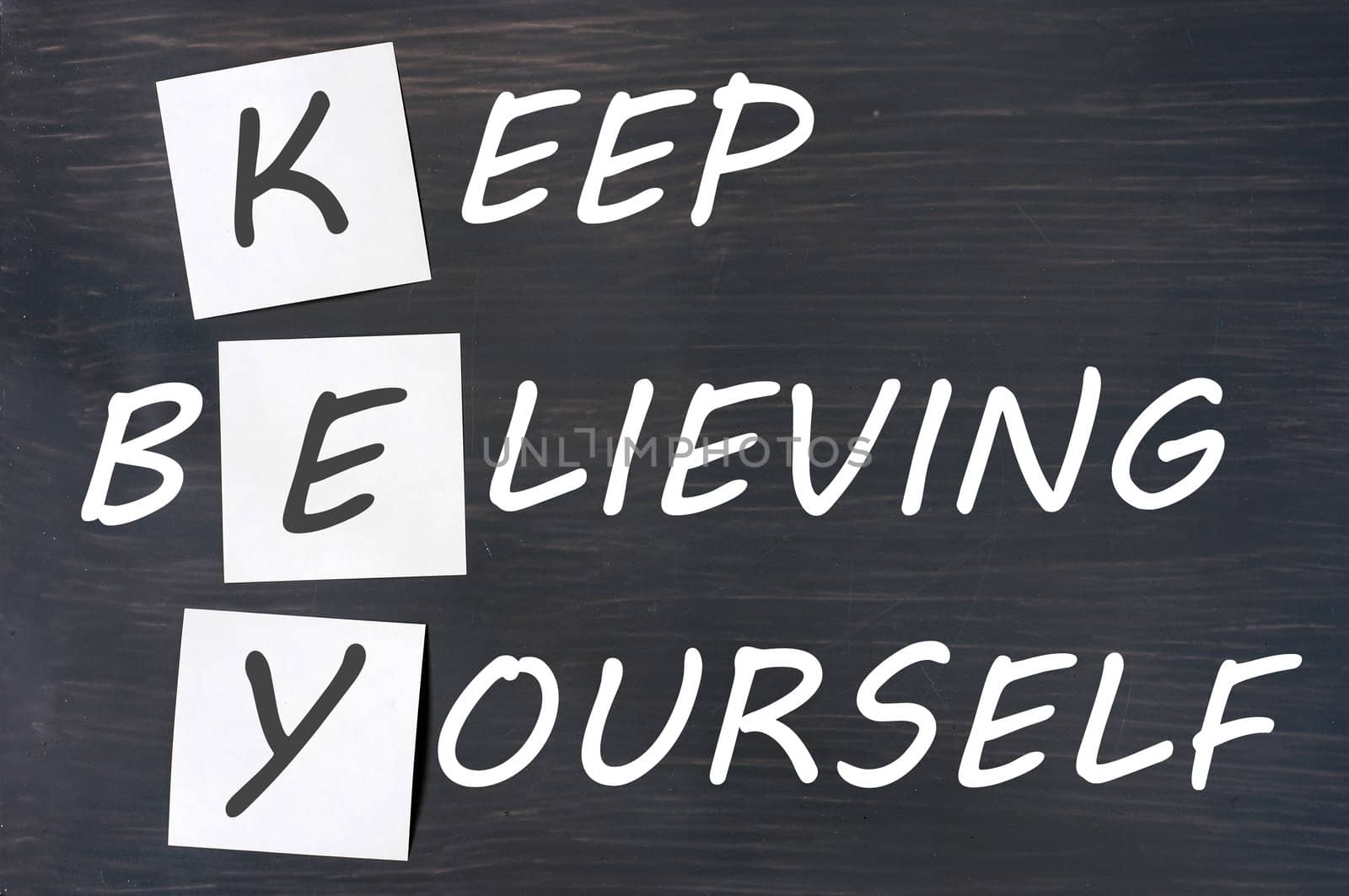 Acronym of KEY for Keep Believing Yourself written in chalk on a smudged wooden blackboard