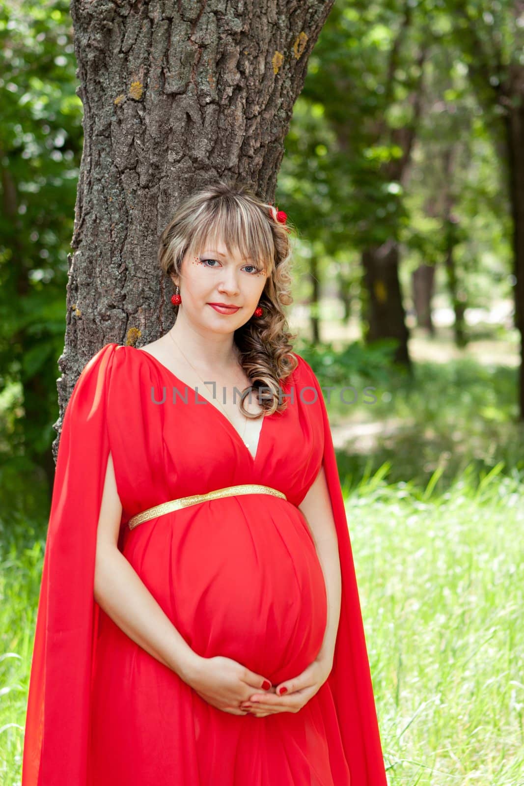 A pregnant woman standing next to a tree.