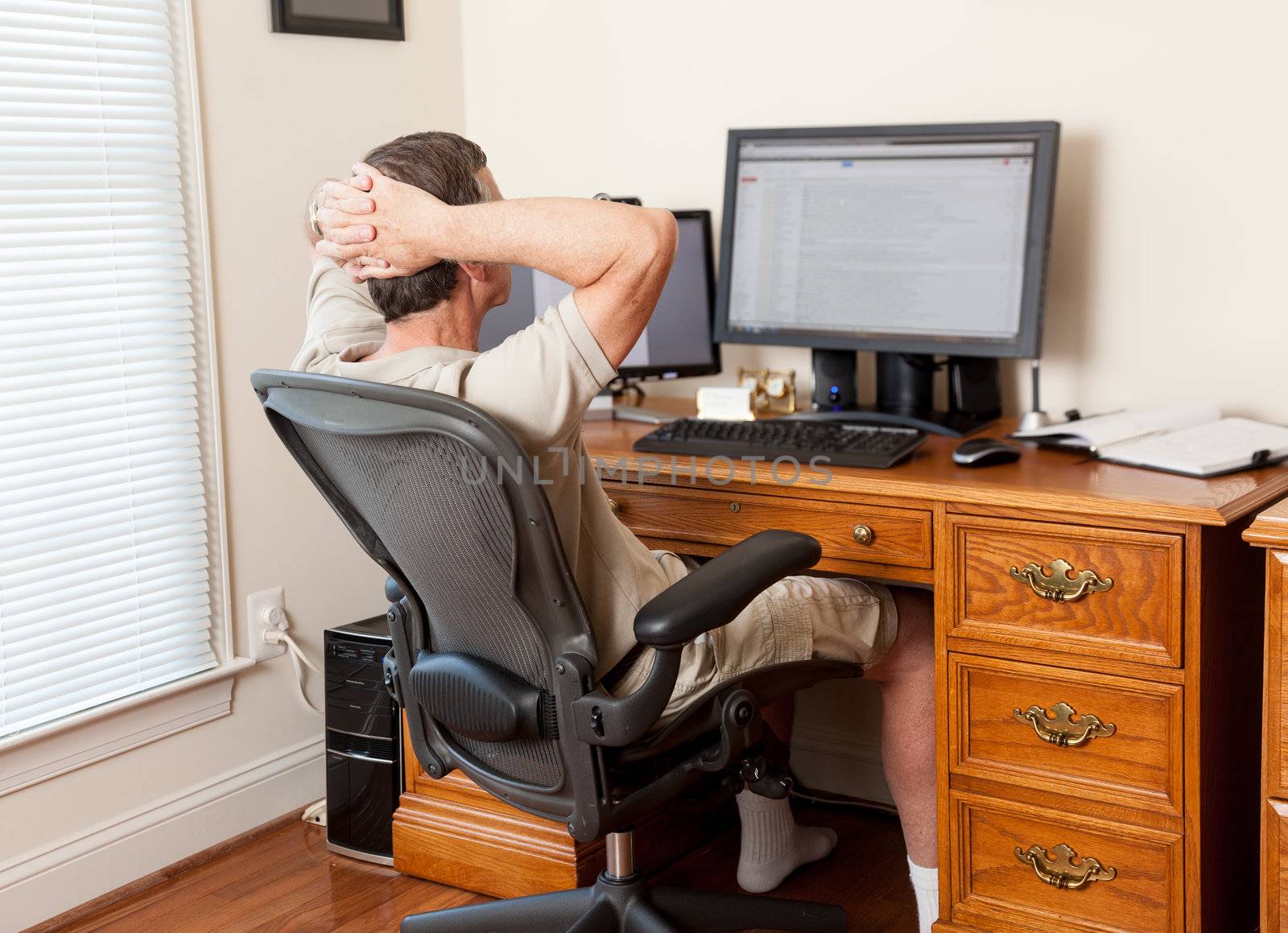 Senior caucasian man working from home in shorts with desk with two monitors