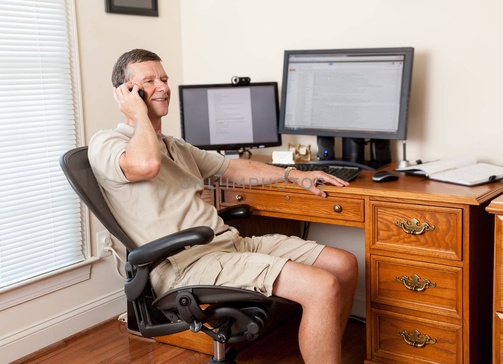 Senior caucasian man working from home in shorts with desk with two monitors