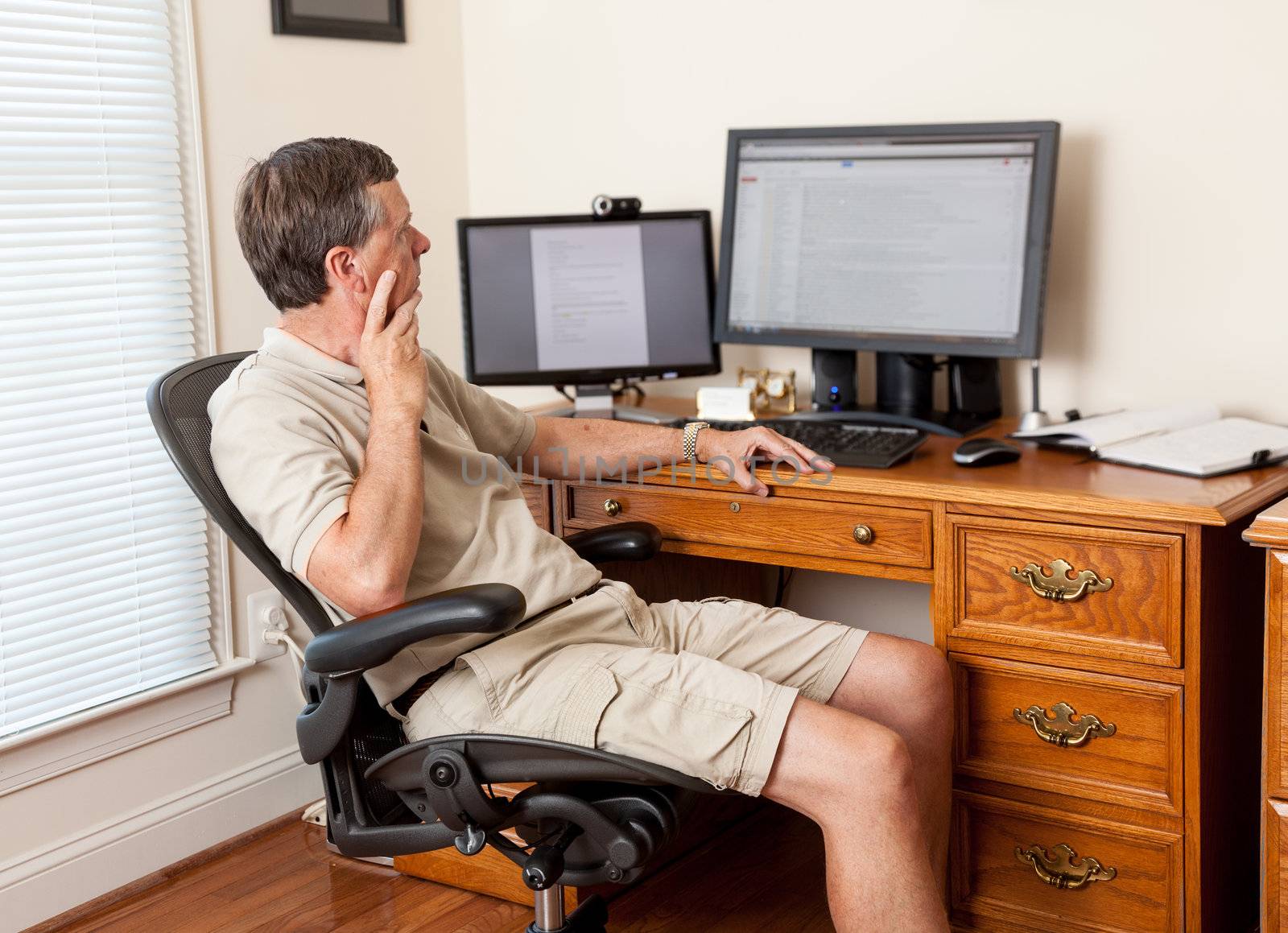 Senior caucasian man working from home in shorts with desk with two monitors