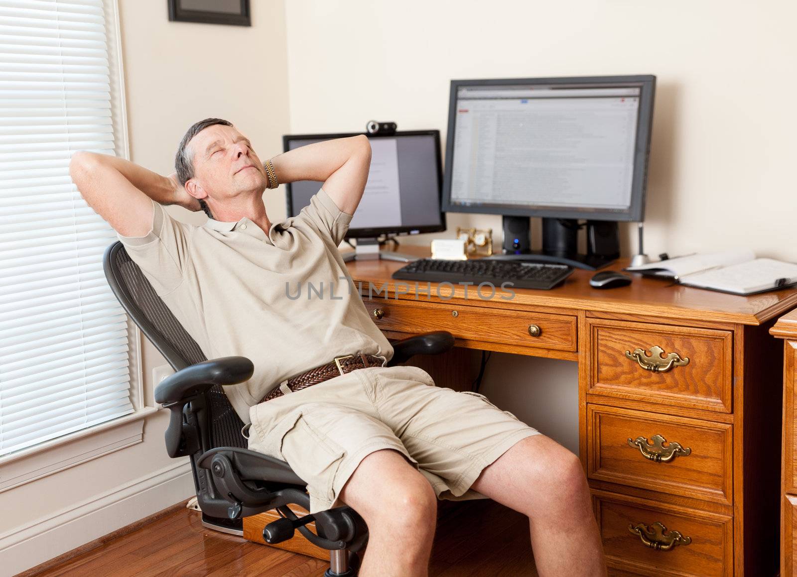 Senior caucasian man working from home in shorts with desk with two monitors