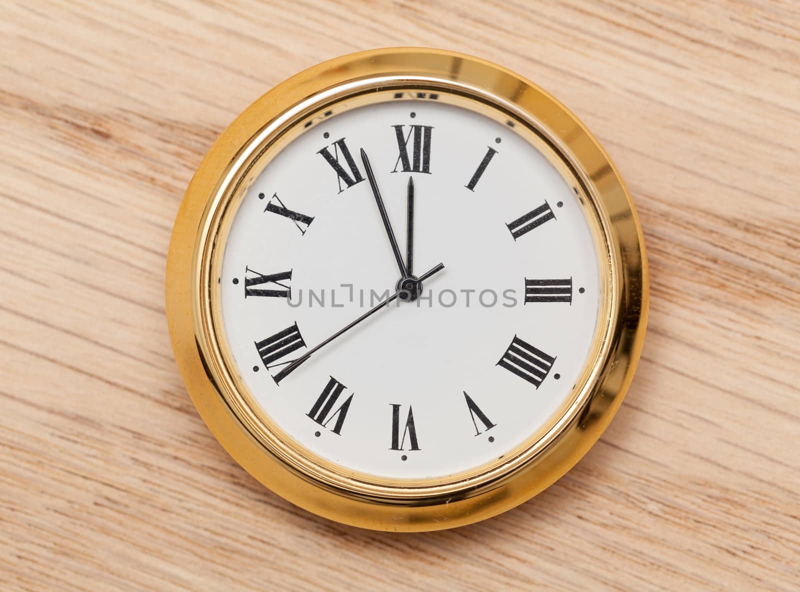 Small gold colored clock almost at midnight and laying on a wooden table
