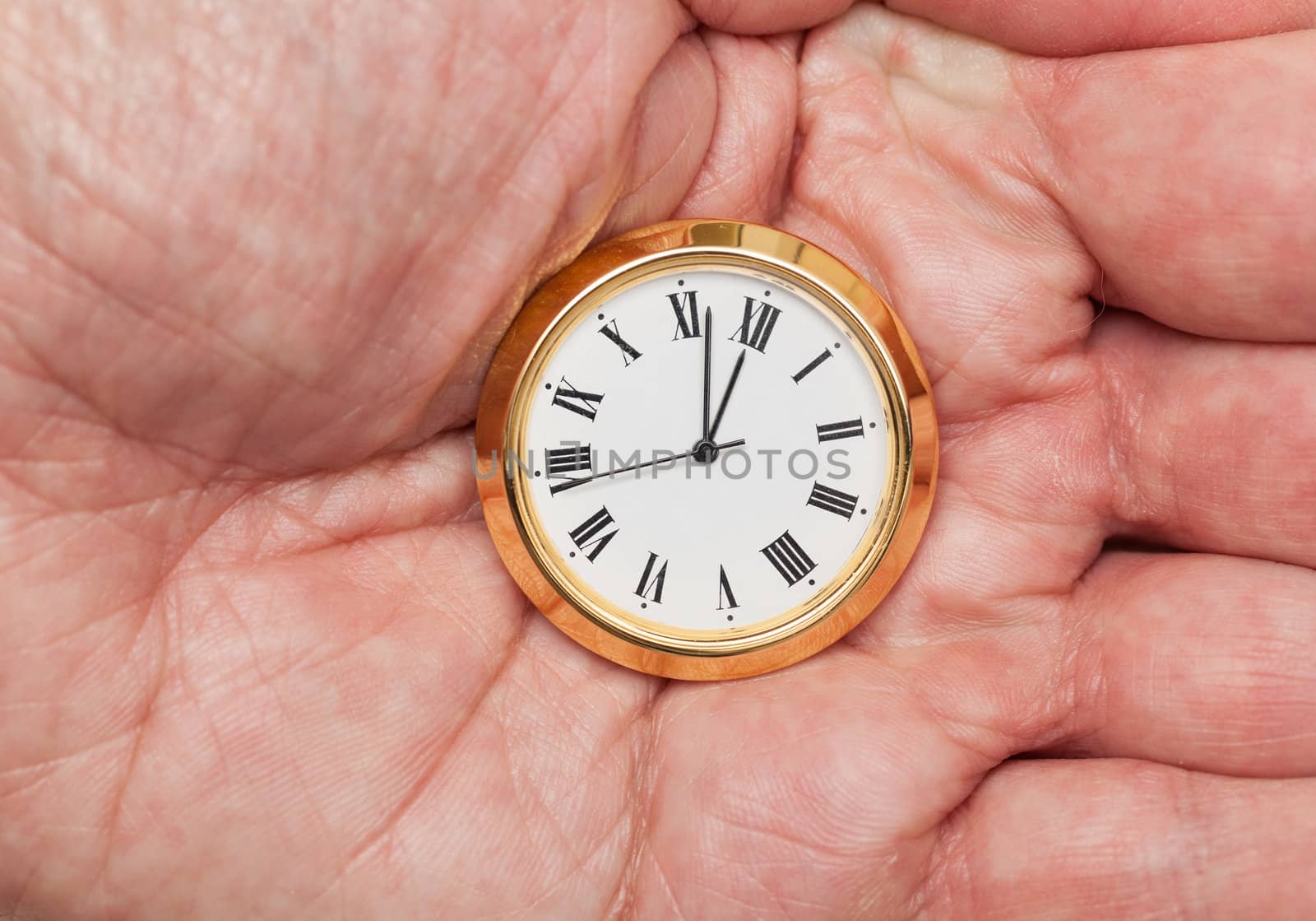 Small gold colored clock almost at midnight held in palm of hand