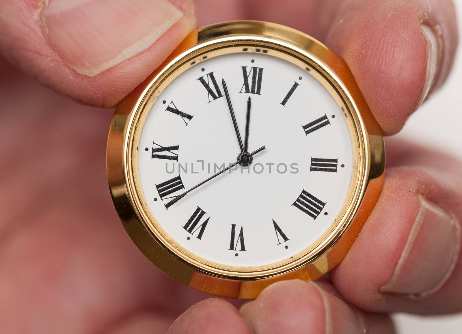 Small gold colored clock almost at midnight held by tips of fingers