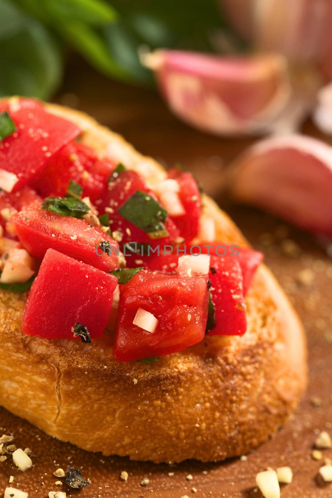 Fresh homemade crispy Italian antipasto called Bruschetta topped with tomato, garlic and basil on wooden board (Selective Focus, Focus on the tomato piece in the front) 