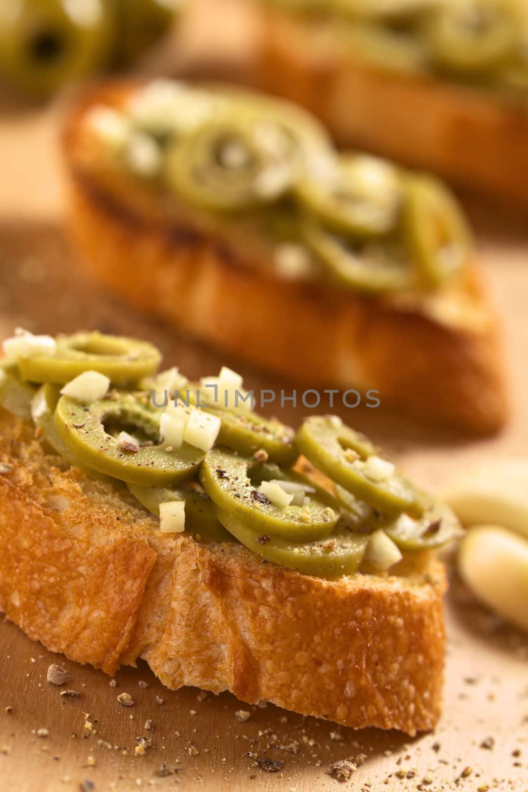 Fresh homemade crispy Italian antipasto called Bruschetta topped with green olive slices and garlic seasoned with ground pepper (Selective Focus, Focus on the olives in the front) 