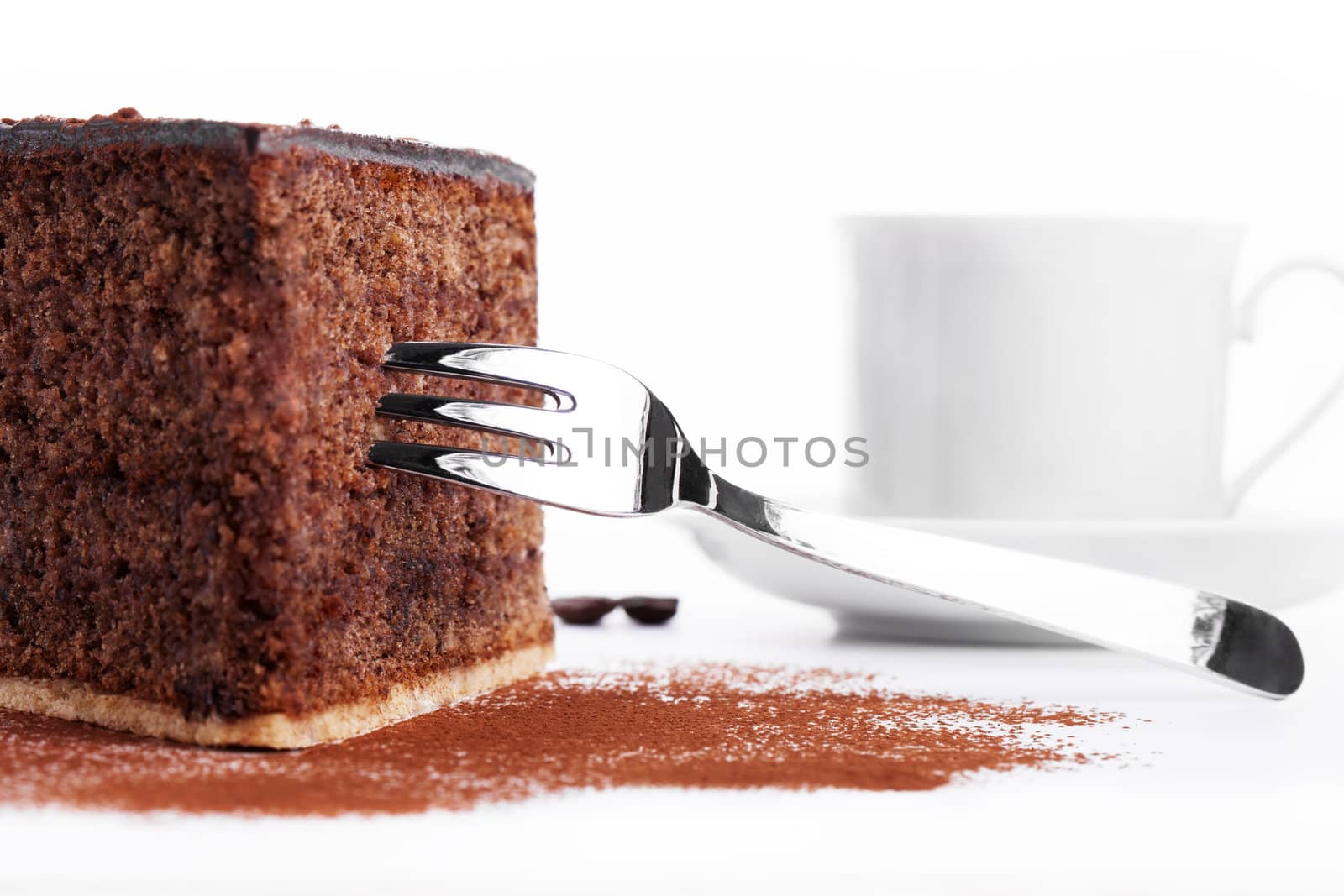 closeup of a chocolate cake with a fork and a cup of coffee in background on white background