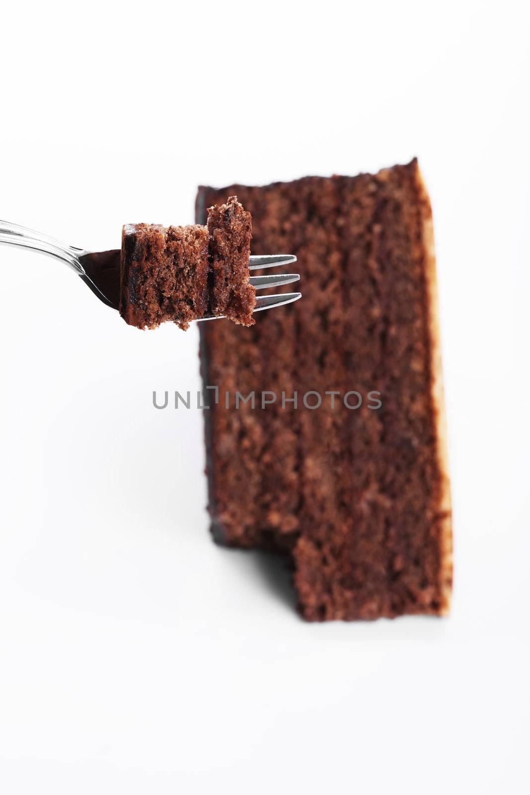 piece of a chocolate cake on a fork over a chocolate cake on white background