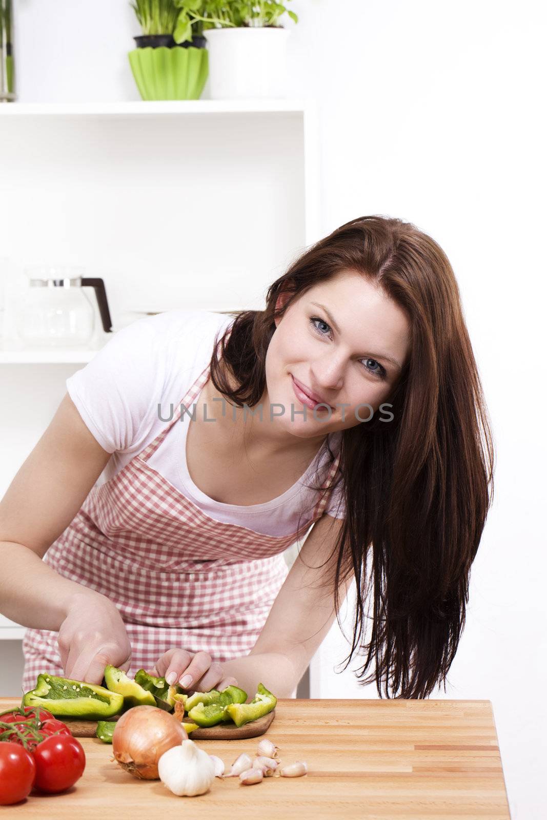 young woman in kitchen cutting green paprika
