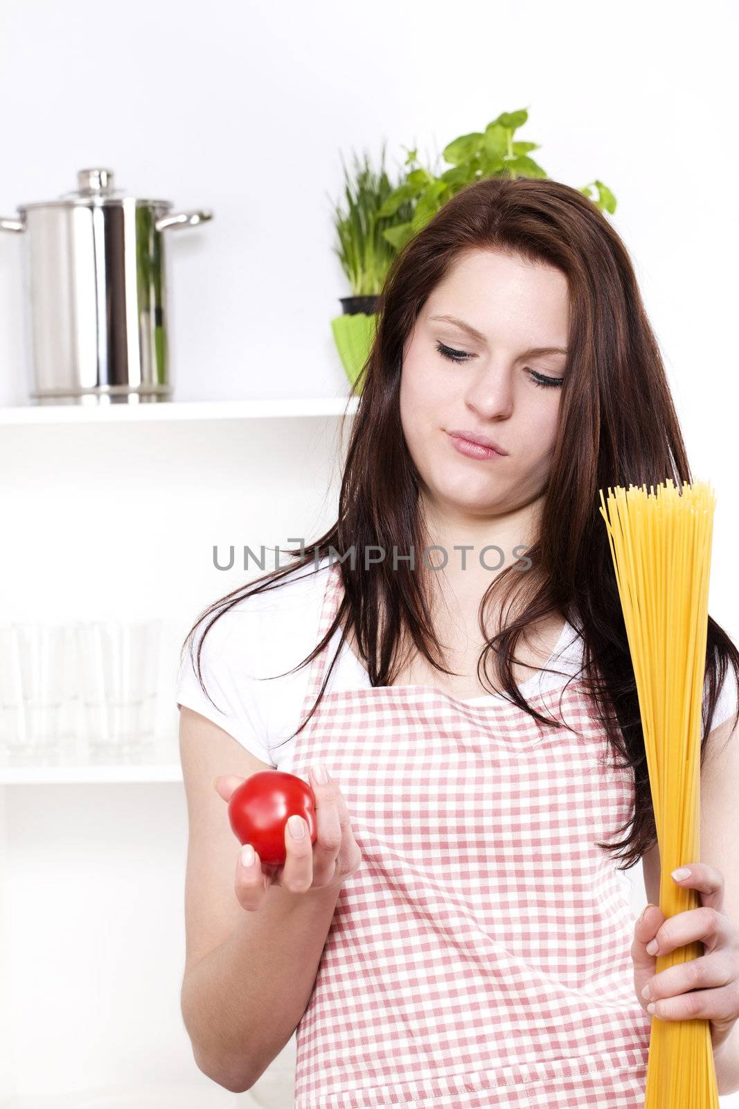 young woman holding spaghetti and tomato looking at the tomato